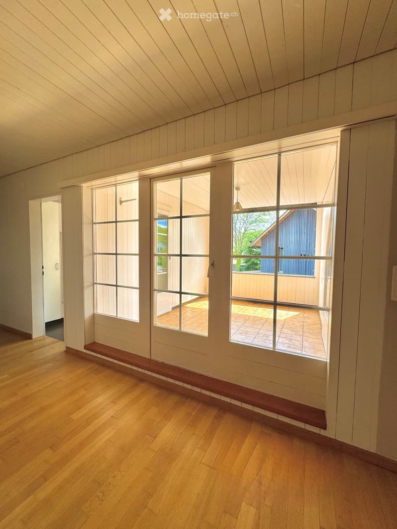 Empty room with wooden flooring, white walls, large windows, and a door leading to an outdoor area.
