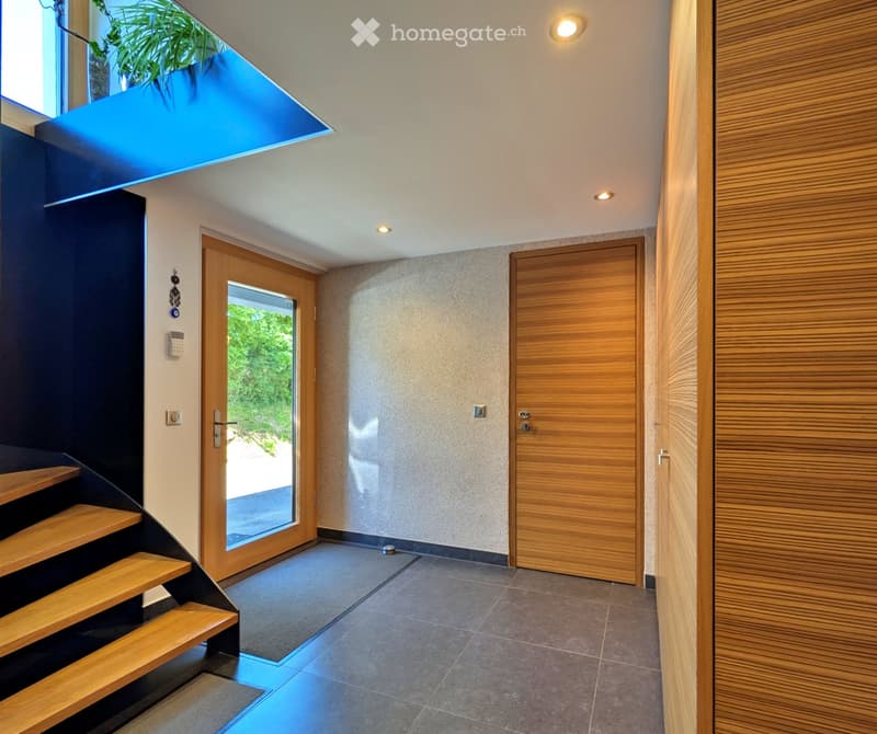 Modern hallway with wooden stairs, glass door, and recessed lighting. Features a sleek design with a combination of dark and light tones.