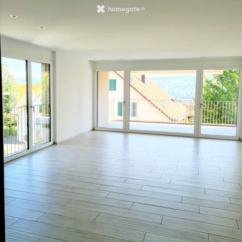 Completely empty room with light wooden flooring, large glass sliding doors leading to a balcony, and white walls.