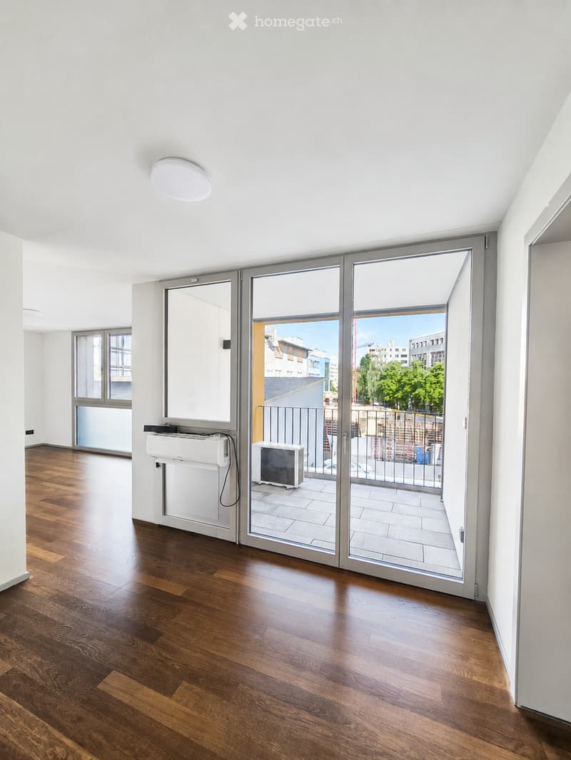 Empty room with wooden flooring, white walls, large sliding glass doors leading to a balcony, and a visible radiator and air conditioning unit.