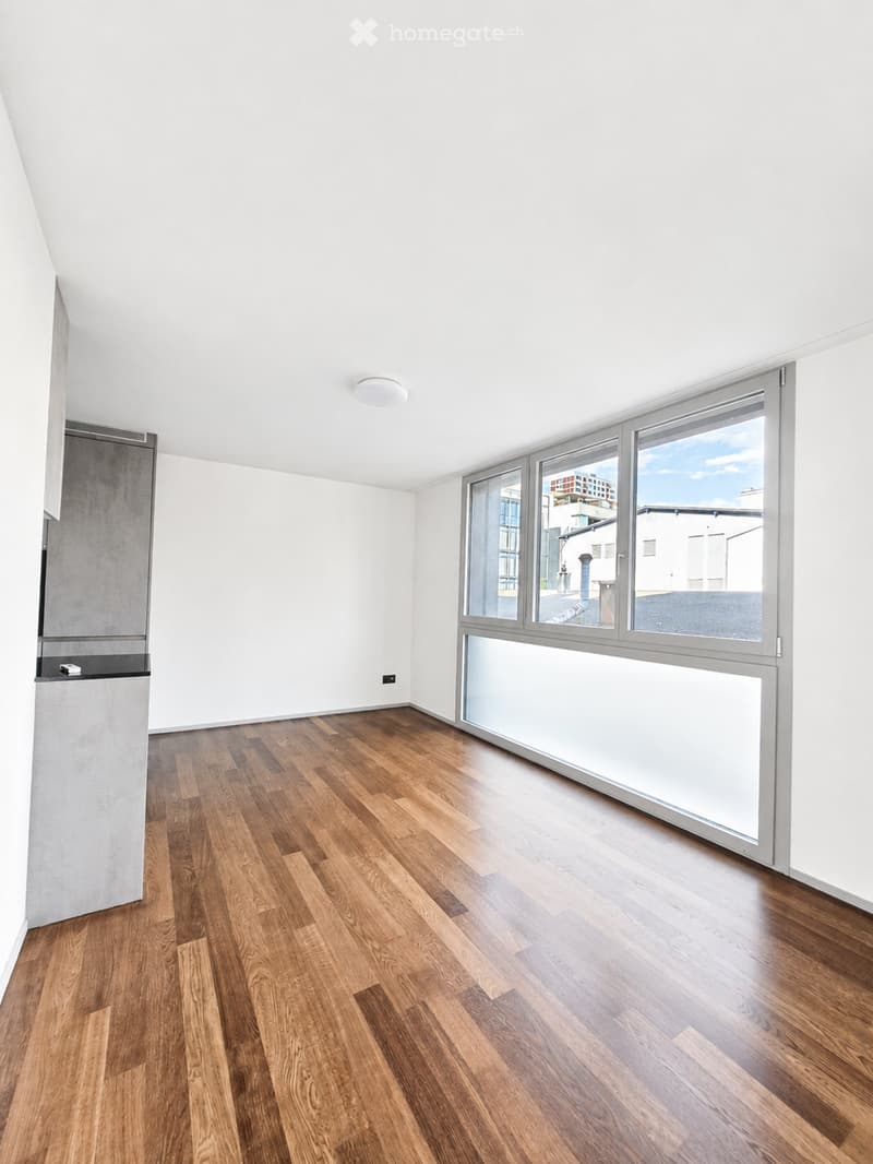 Empty room with wooden flooring, white walls, large windows, and a modern ceiling light fixture.