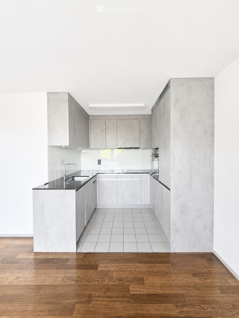 Modern, minimalist kitchen with white cabinets, stainless steel sink, and wooden flooring. No furniture or appliances visible.