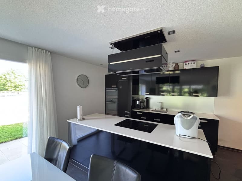 Modern kitchen with white island, black cabinets, induction cooktop, and stainless steel appliances.