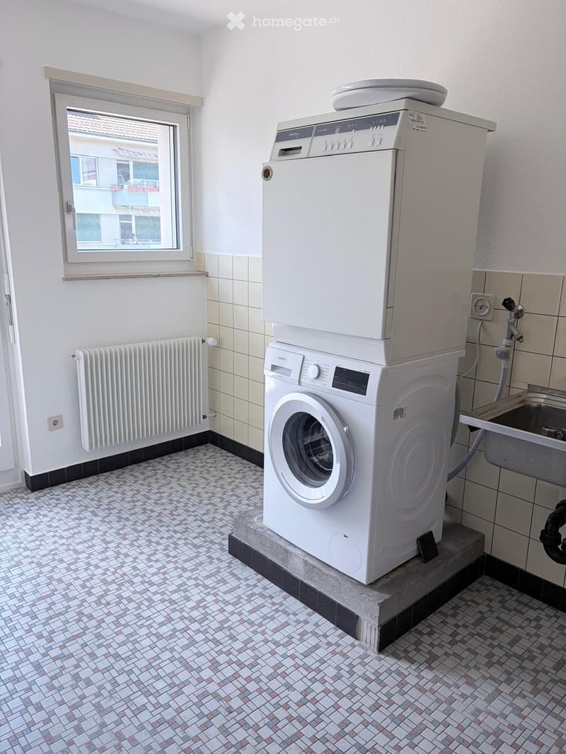Bathroom with tiled walls and floor, featuring a washing machine and dishwasher stacked together, a radiator, and a sink.