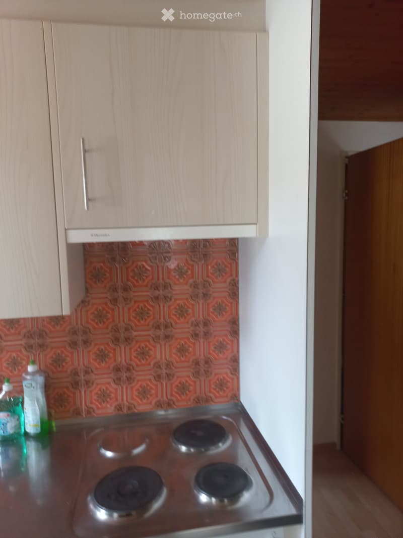 kitchen with stove, kitchen cabinets, tiled wall, cleaning products on the counter
