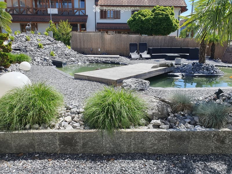 Garden area with a small pond, wooden deck, lounge chairs, and decorative rocks and plants.