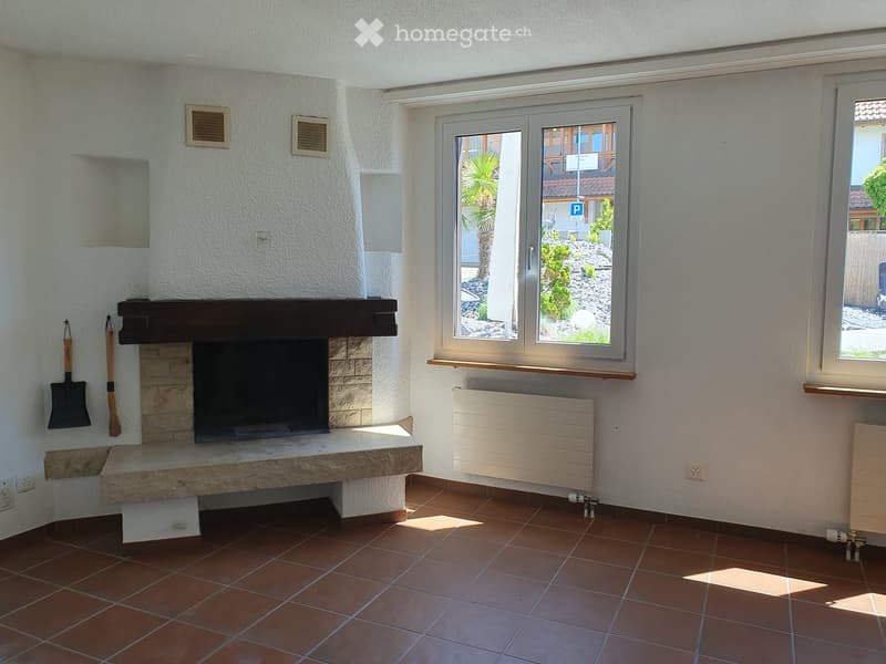 Empty room with tiled floor, fireplace, large window, radiator, and two shovels on the wall.