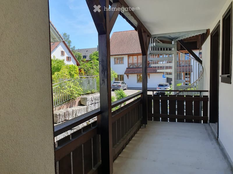 Balcony with wooden railing, stone wall, and view of neighboring houses and parked cars.