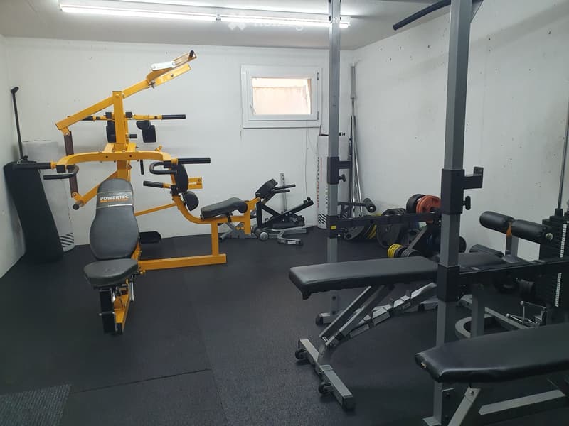A well-equipped home gym with a weight bench, a yellow weight machine, a punching bag, and various weight plates.
