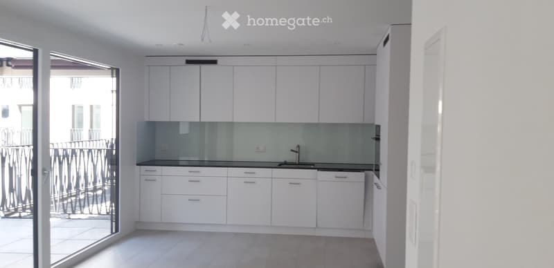 Modern, minimalist kitchen with white cabinets, a central island, and a sleek glass backsplash. Features a large sliding glass door leading to a balcony.