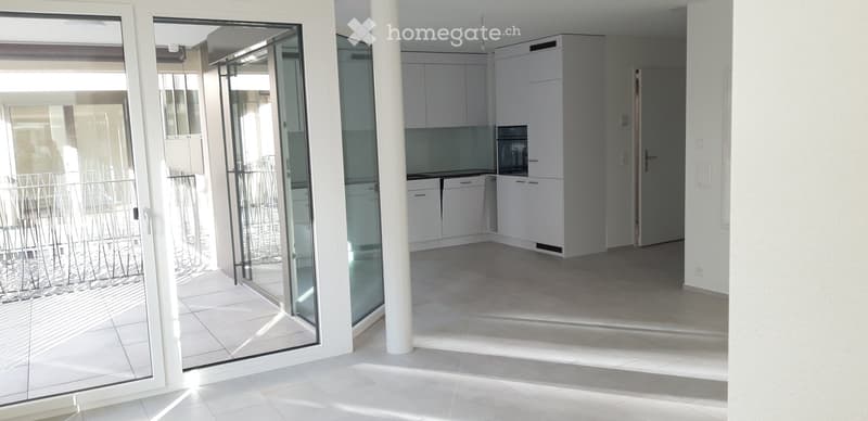 Empty kitchen with white cabinets, a microwave, and a tiled floor, connected to a balcony through large glass doors.