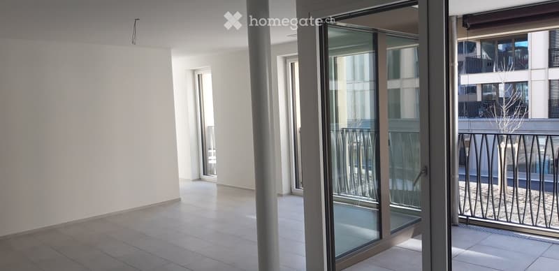 Modern balcony with large glass sliding doors, tiled floor, and metal railing overlooking neighboring buildings.