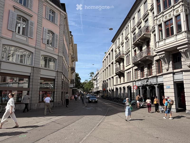 A bustling urban street lined with multi-story buildings, featuring shops, pedestrians, and parked bicycles.