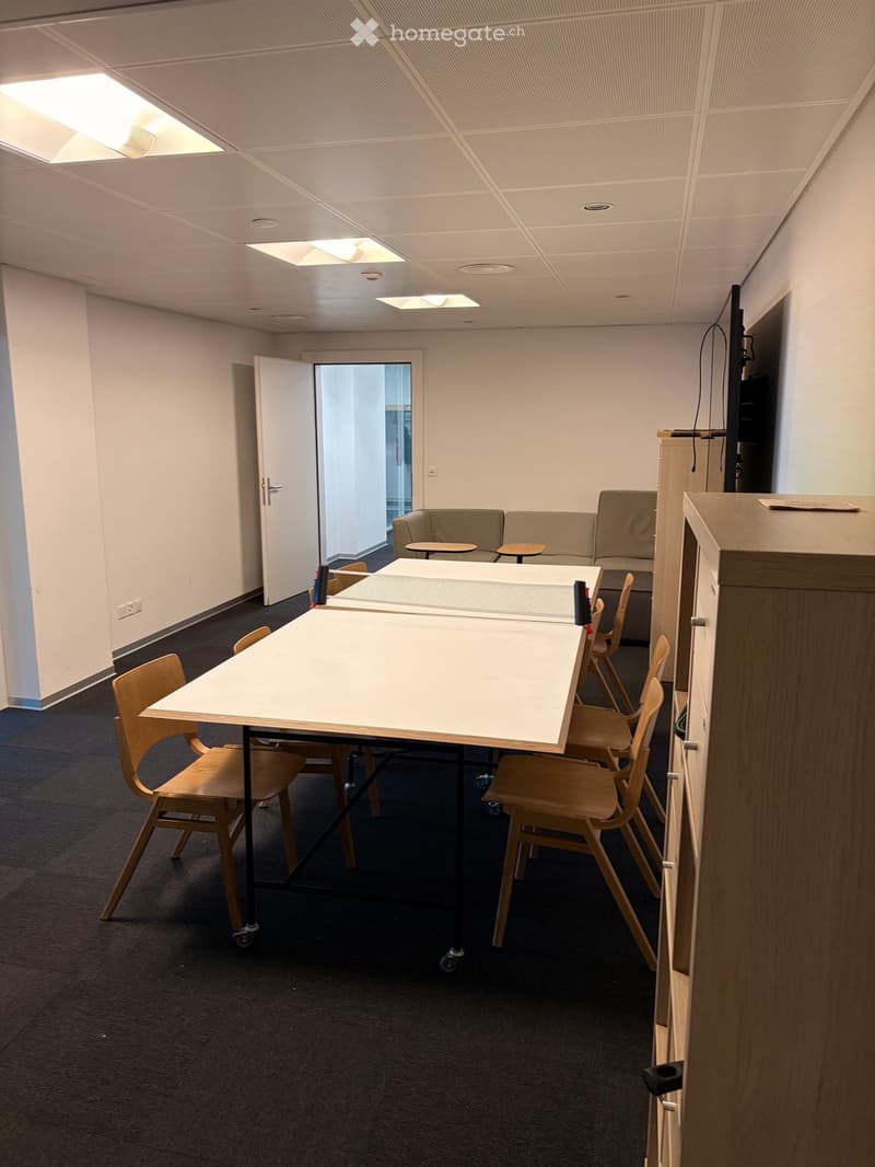 A modern break room with a ping pong table, chairs, and a small sofa area.