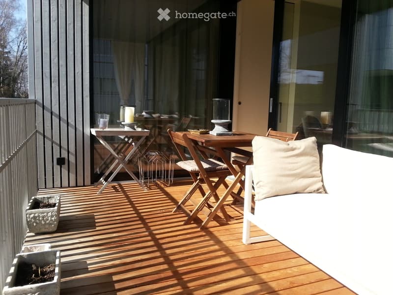 A wooden deck with a white sofa, a small table with chairs, candles, and a flower pot.