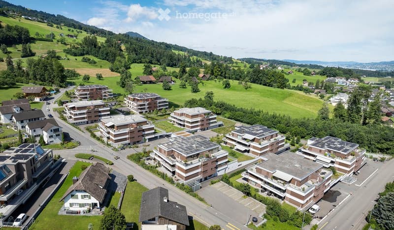 Aerial view of a residential area with multiple apartment buildings, houses, and green spaces, surrounded by hills and trees.