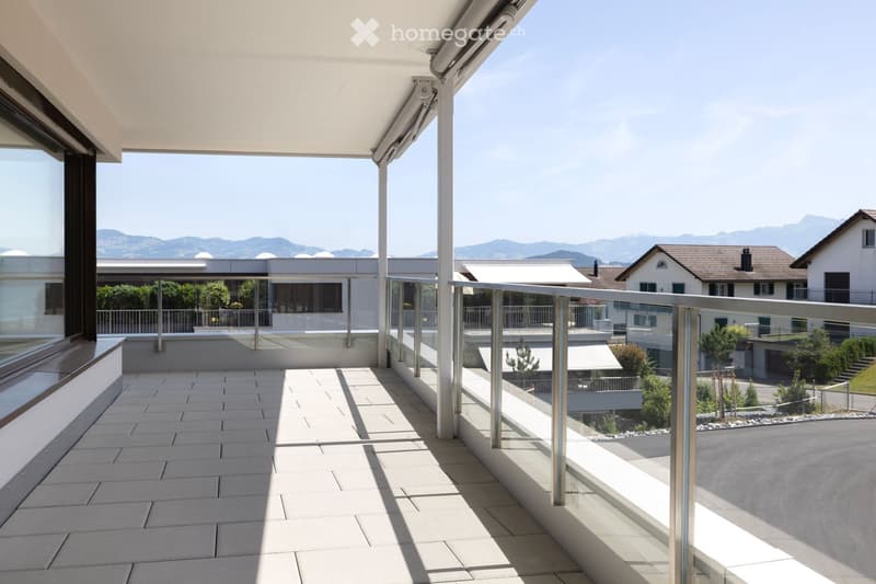 Modern balcony with tiled floor, glass railing, and retractable awning, overlooking a residential area with mountains in the background.