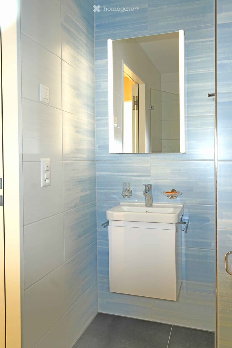 Bathroom with blue tiles, white sink, mirror, and glass shelf
