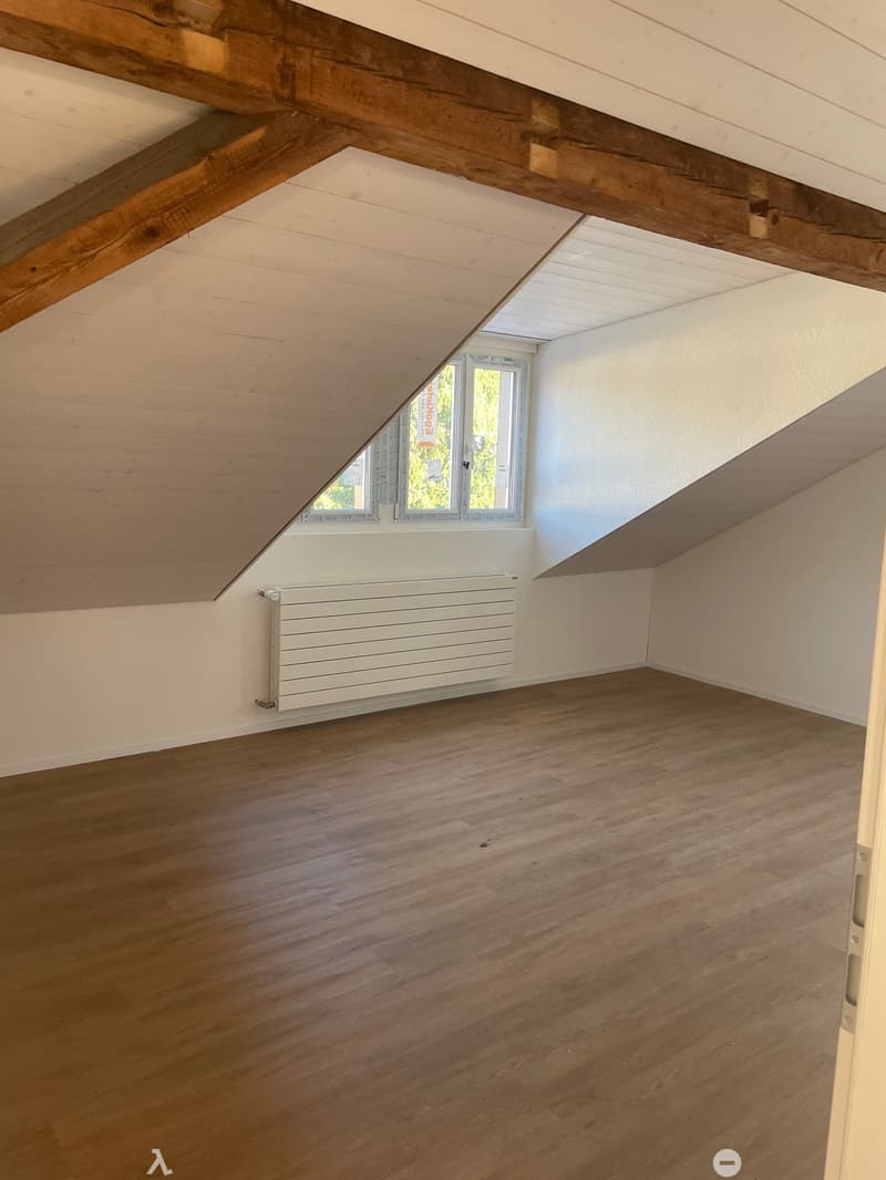 Unfurnished Room. Empty attic room with wooden floor, white walls, exposed wooden beams, and a single window with white frame and blinds.
