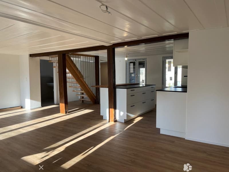 Kitchen. Bright, open kitchen with white cabinets, a central island, and wooden flooring. Natural light streams in, creating sunlit patterns on the floor.