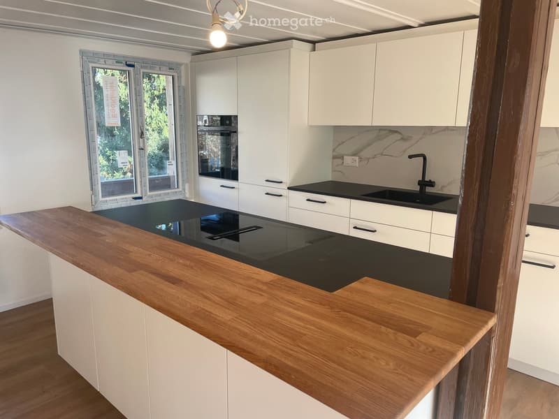 Kitchen. Modern kitchen with white cabinets, wooden countertop, black sink, and large window offering a view of greenery.
