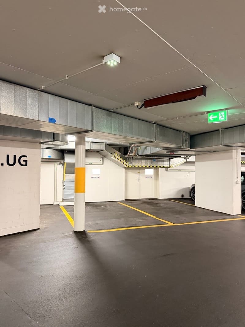 Underground parking area with marked parking spaces, pillars, and an emergency exit sign.