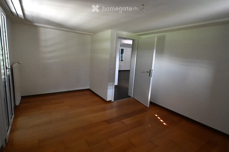 Empty room with wooden flooring, white walls, and a partially open door leading to another room.