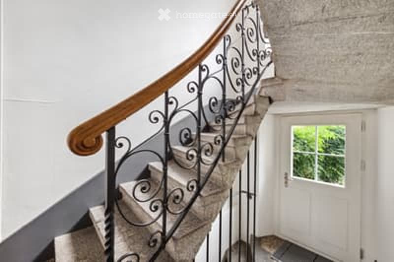 Staircase with wooden handrail and wrought iron balustrade, leading to a white door with a glass panel.