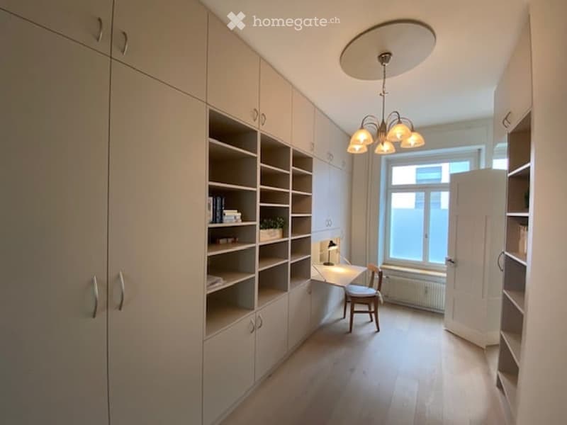 Bright, modern room with built-in white cabinetry and shelving, a small desk with a chair, a hanging light fixture, and a potted plant on the shelf.