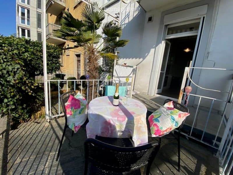 Balcony with a round table, chairs, and decorative cushions, overlooking a palm-lined street.