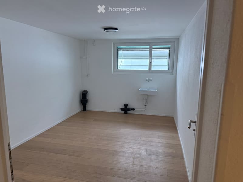 Empty room with wooden flooring, white walls, a window, a sink, and a heating pipe.