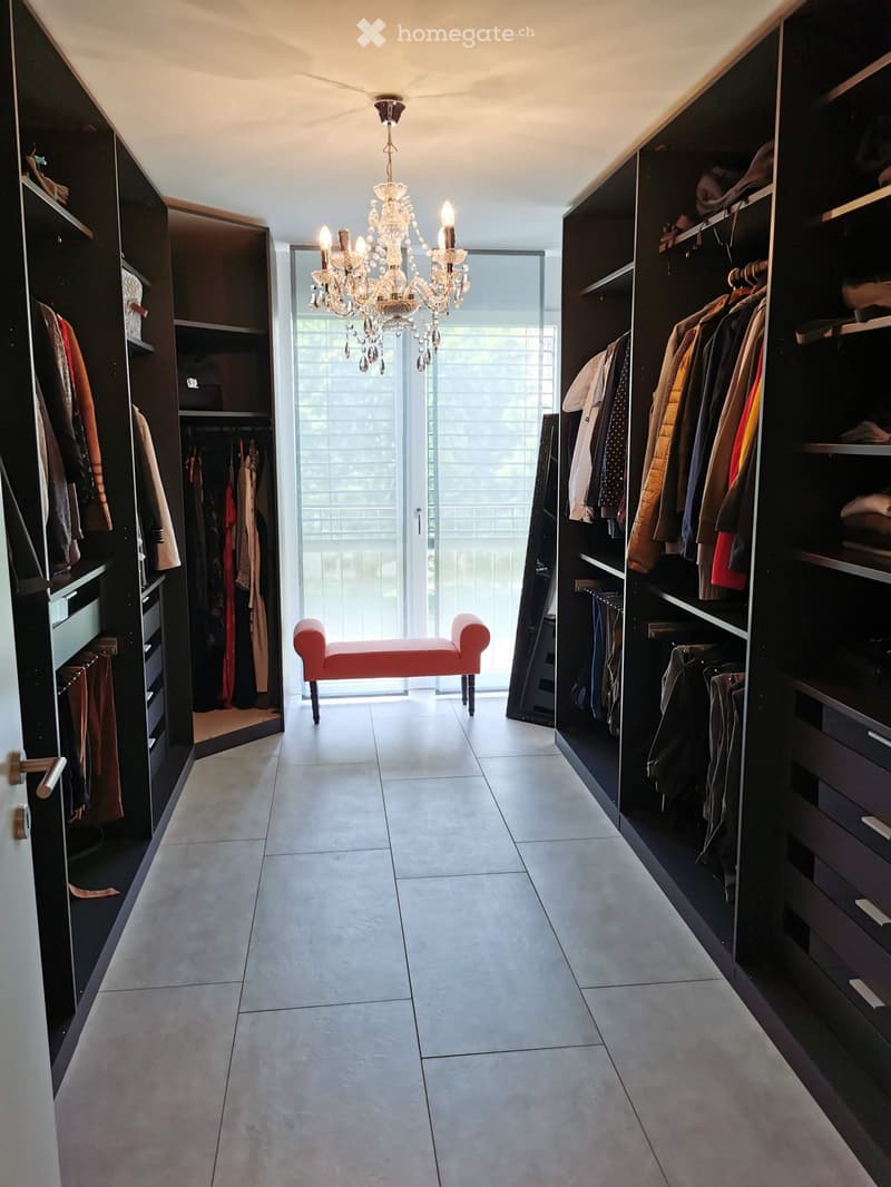 Spacious walk-in closet with built-in wardrobes, a red bench, and a chandelier hanging from the ceiling.