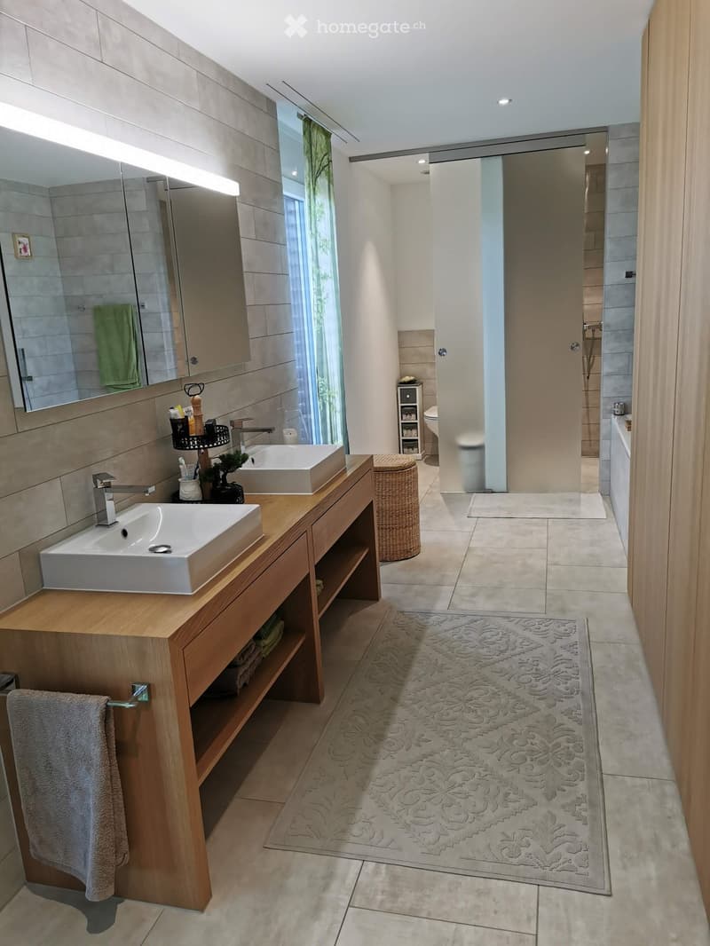 Modern bathroom with double sinks, large mirror, wooden vanity, tiled walls, and a separate shower area.