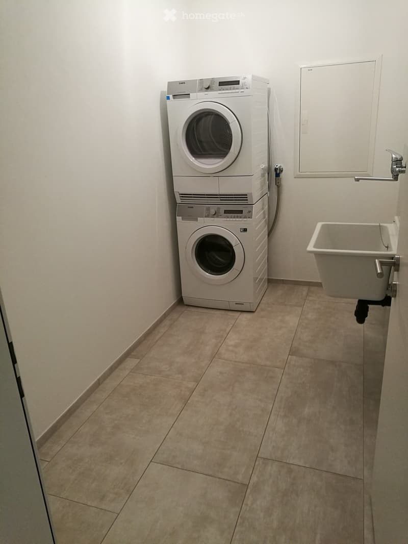 A small bathroom with a washing machine, dishwasher, and a sink. The floor is tiled, and the walls are white.