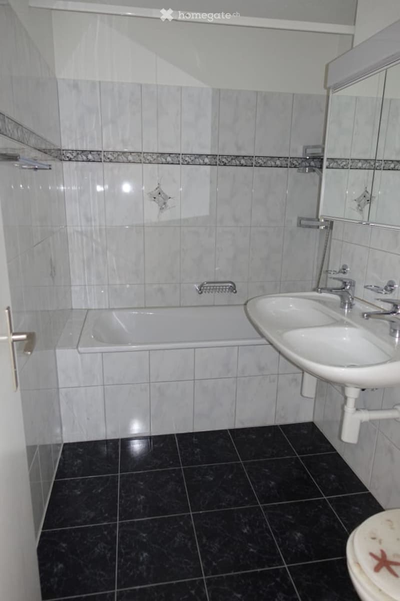 Modern bathroom with white marble tiles, black tiled floor, bathtub, double sink, and mirror.