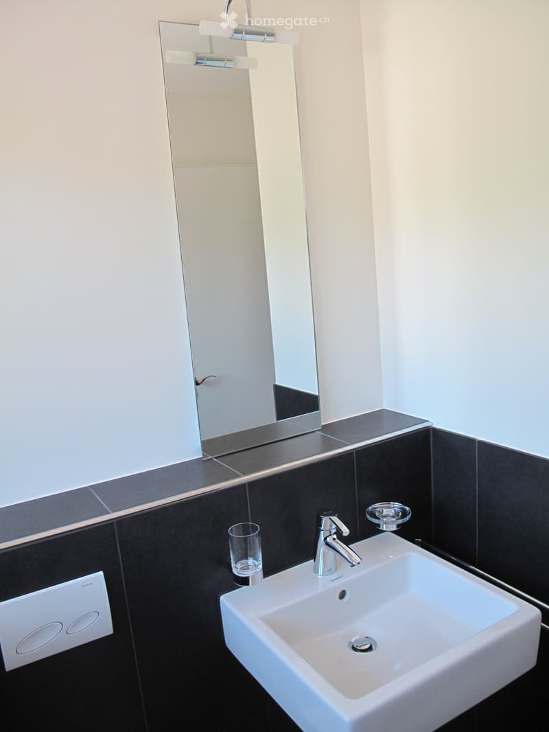 Modern bathroom with a white sink, chrome faucet, large mirror, and a glass on the counter.