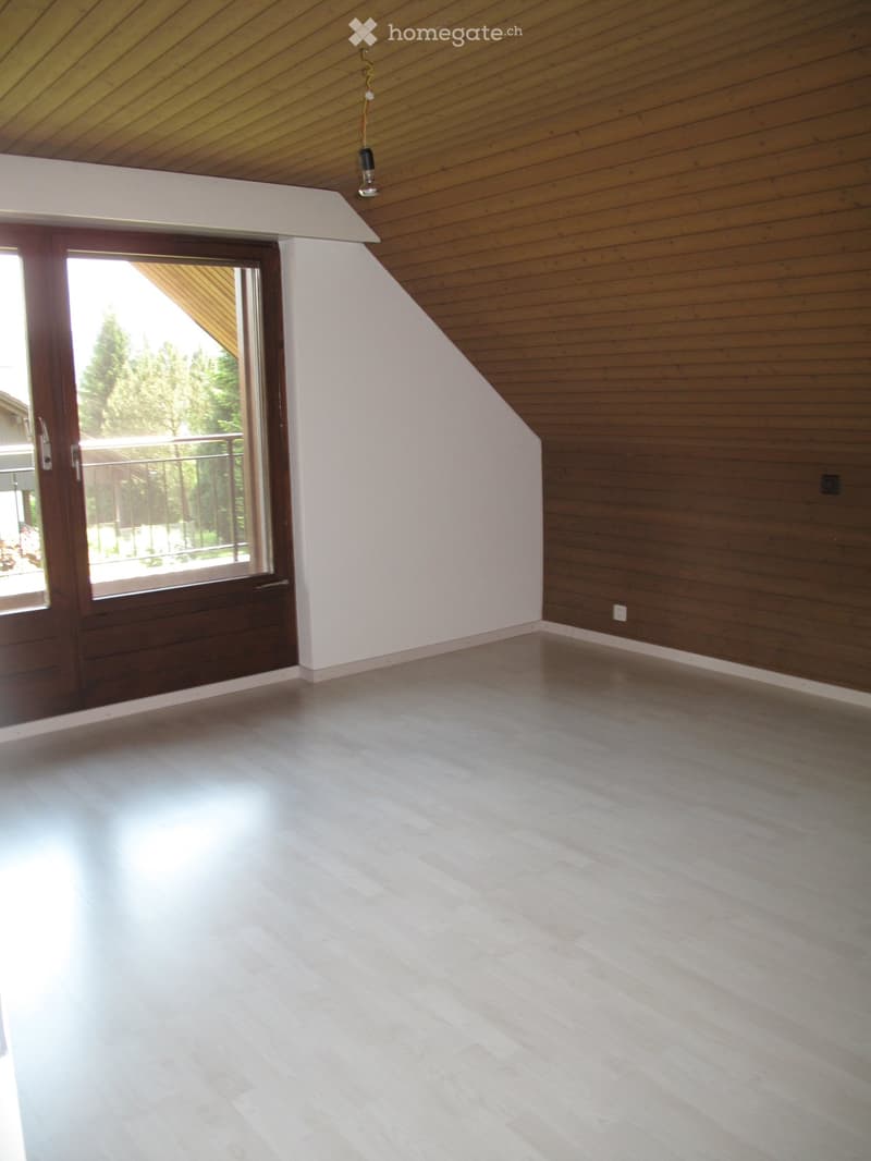 Empty room with wooden walls, white ceiling, and large window with wooden frame and glass door leading to a balcony.