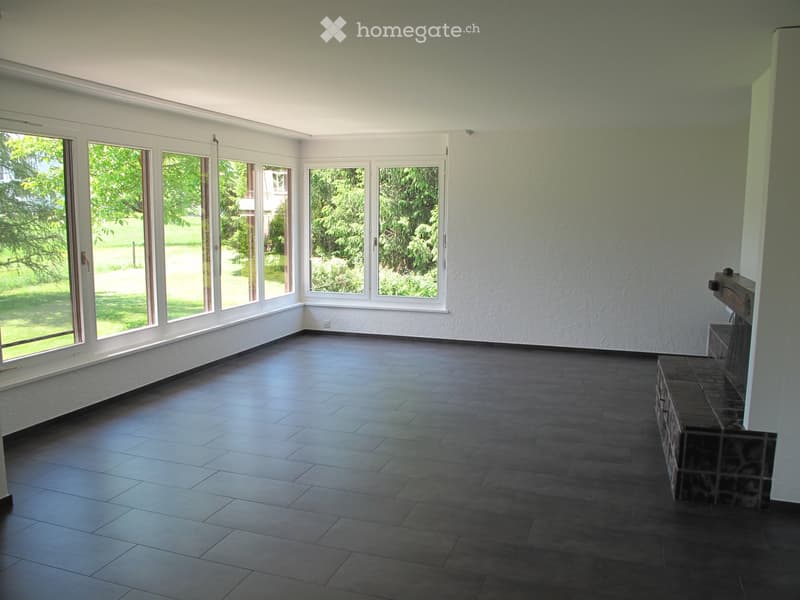 Empty room with large windows, dark tiled floor, and a fireplace structure in the corner.