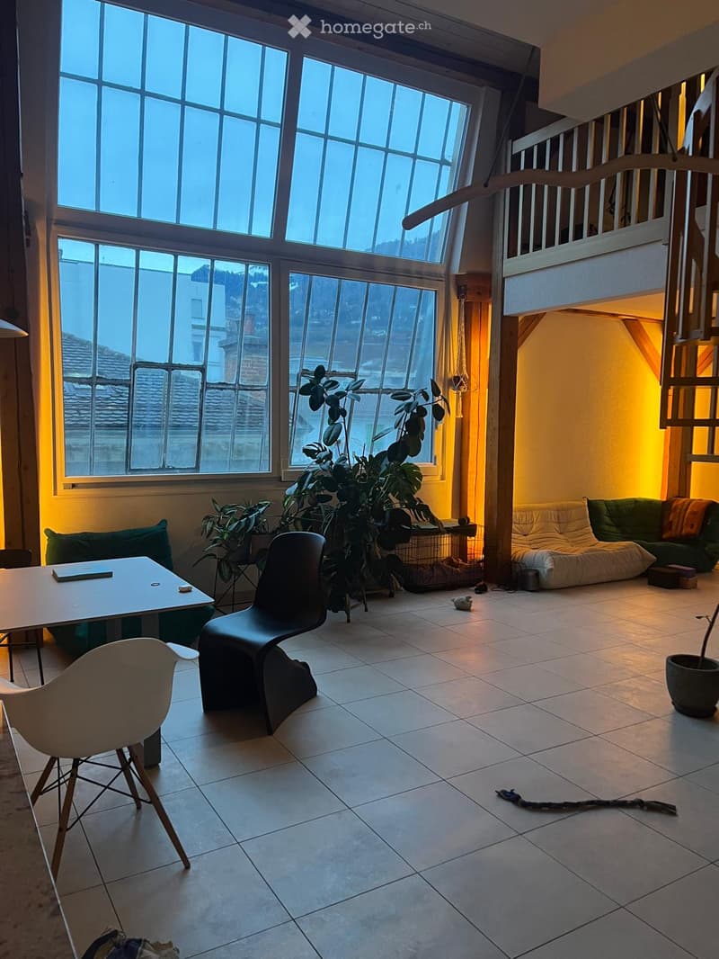 Bright living room with large windows, tiled floor, modern furniture including a sofa, chairs, and a table, with plants and a cozy seating area.