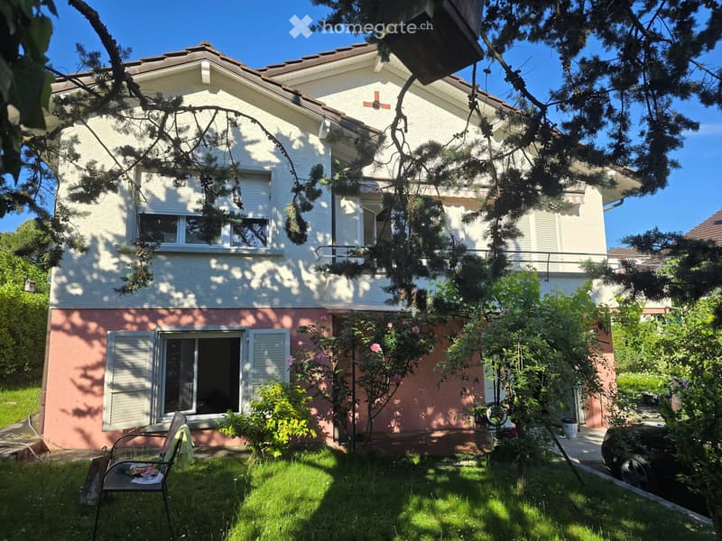 Two-story house with white and pink exterior, multiple windows, and a small garden area with a chair and plants.