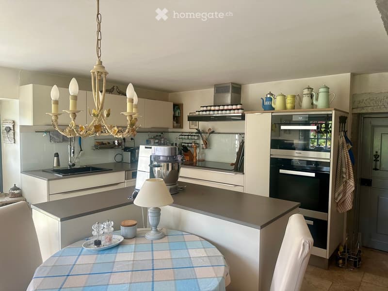 Modern kitchen with white cabinets, grey countertops, a central island, a chandelier, and a dining area with a table and chairs.
