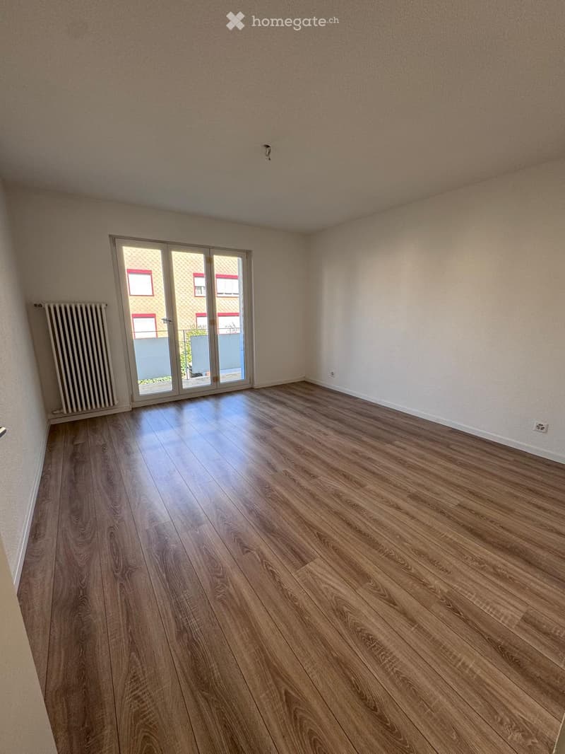 Empty room with wooden flooring, white walls, and a sliding glass door leading outside.