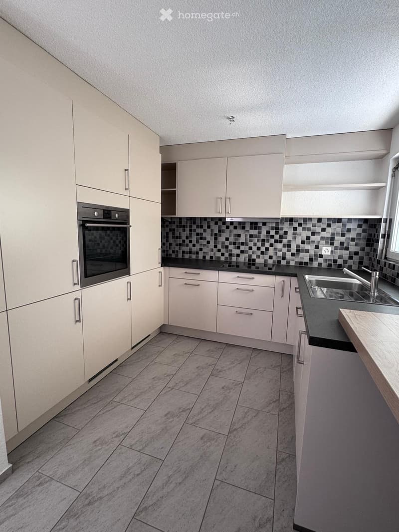 Modern kitchen with light-colored cabinets, a built-in oven, a sink with a faucet, and a black countertop.