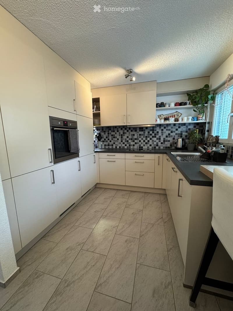 Modern kitchen with white cabinets, black countertops, and a tiled backsplash. Features an oven, sink, and various kitchen appliances.