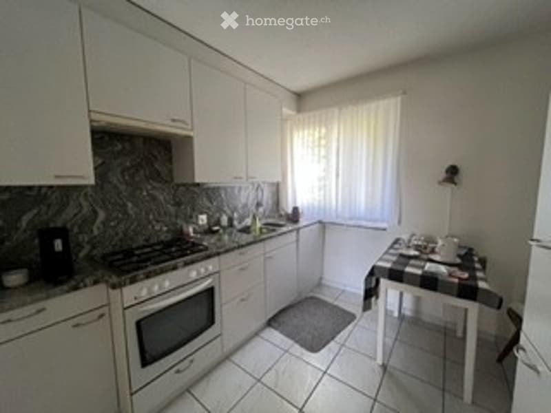 Bright kitchen with white cabinets, a stove, oven, refrigerator, and a small dining area with a table and chairs.