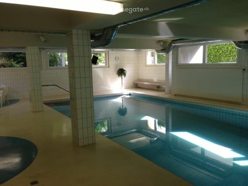 Indoor swimming pool area with tiled walls, a small bench, and windows letting in natural light.