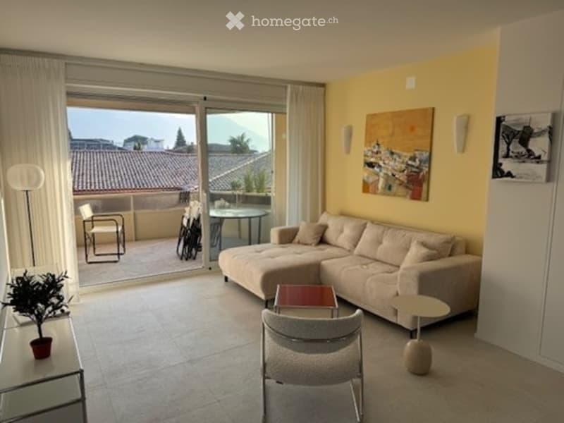Bright living room with large sliding glass doors opening to a balcony, yellow walls, a sectional sofa, coffee table, chairs, and a small table on the balcony.