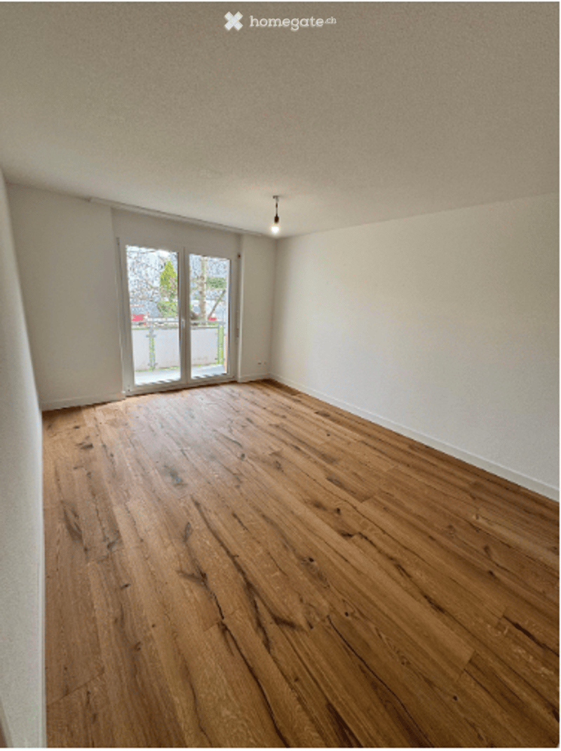 Empty room with wooden flooring, white walls, and large glass doors leading to an outdoor area.