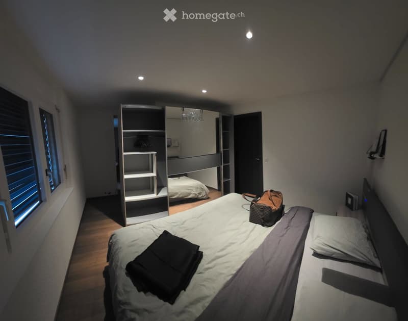 Modern bedroom with a large bed, a wardrobe with mirrored doors, and a backpack on the bed.