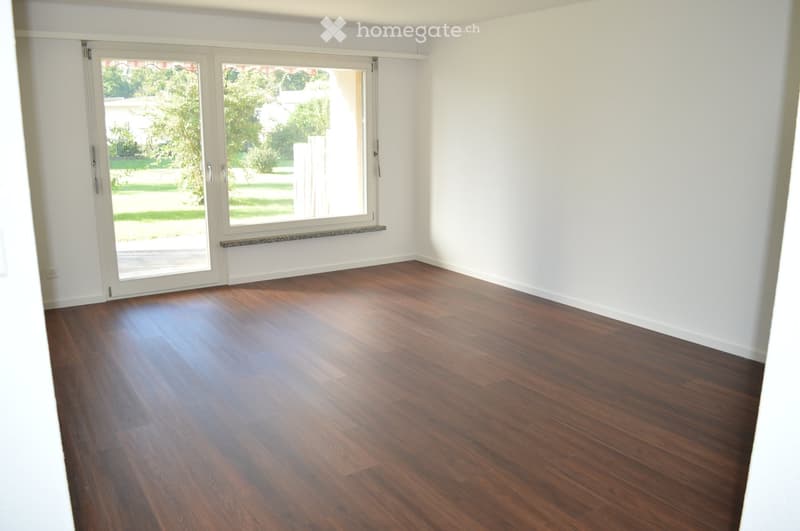Empty room with wooden flooring, white walls, and large sliding glass doors leading to an outdoor area.